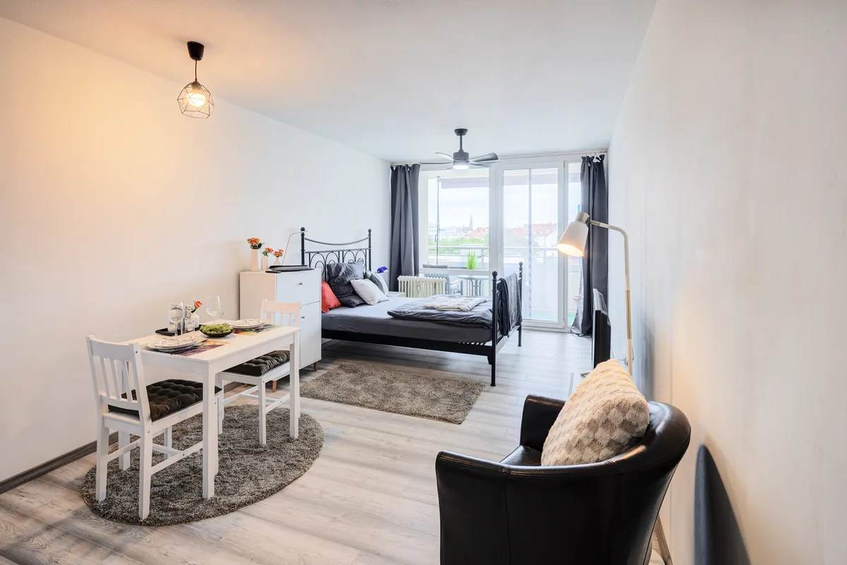Möbliert vermieten in München: möbliertes Apartment mit Bett, Essbereich und Balkon mit Blick über die Stadt